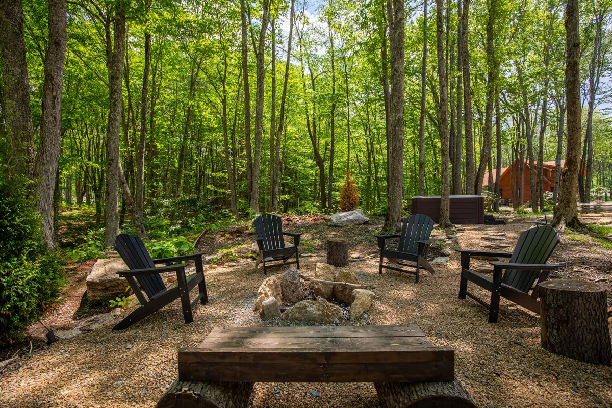 An inviting outdoor communal area with a fire pit surrounded by Adirondack chairs and a wooden bench, nestled among trees. The setting is ideal for campfire gatherings, storytelling sessions, and relaxation, emphasizing a sense of community and connection with nature.