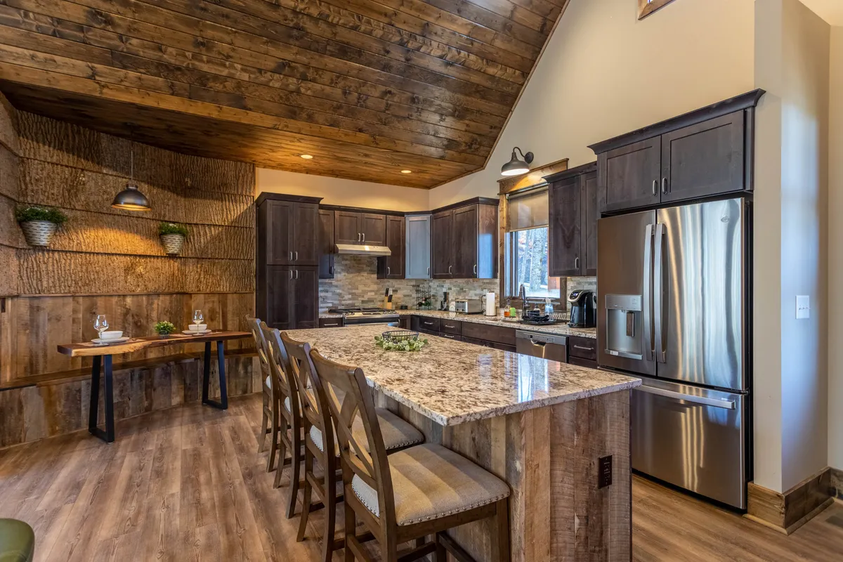 A welcoming kitchen and dining area highlighted by a granite-topped island, rustic wooden ceiling, and a large dining table. The setting is designed for both family cooking and entertaining guests, with ample space for creating and sharing meals together.