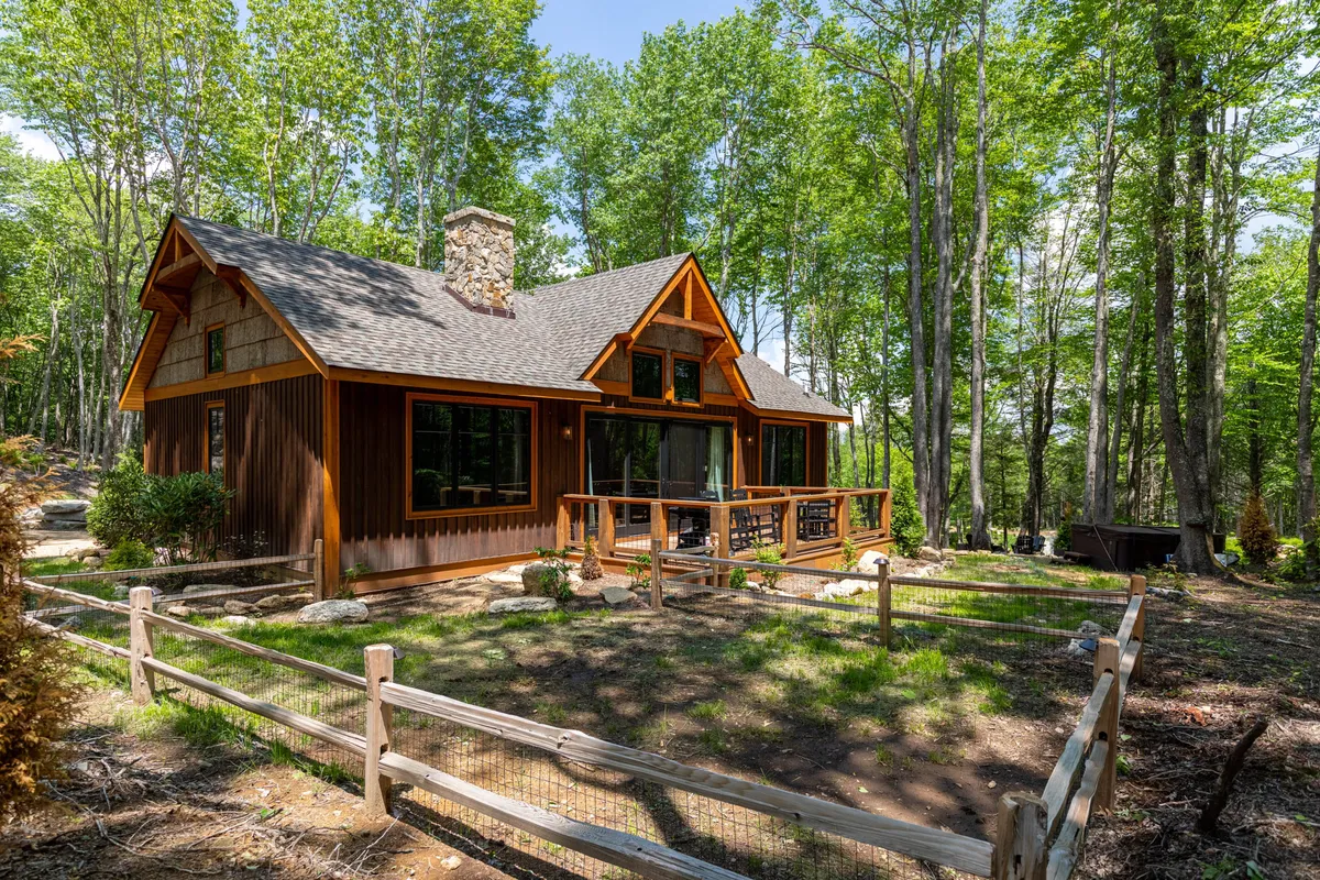 The image features a charming wooden cabin with a stone chimney nestled amid lush trees, a spacious deck inviting outdoor relaxation, and the tranquil backdrop of North Carolina's mountains. The scene exudes a sense of peace and seclusion, perfect for unwinding and connecting with nature.