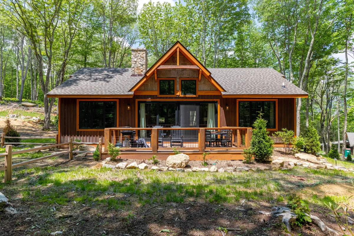 A welcoming view of the cabin's front porch, featuring large windows, a stone chimney, and wooden exterior details. Surrounded by trees and natural scenery, the porch invites guests to relax, enjoy sunsets, or stargaze, setting the tone for a tranquil mountain escape.